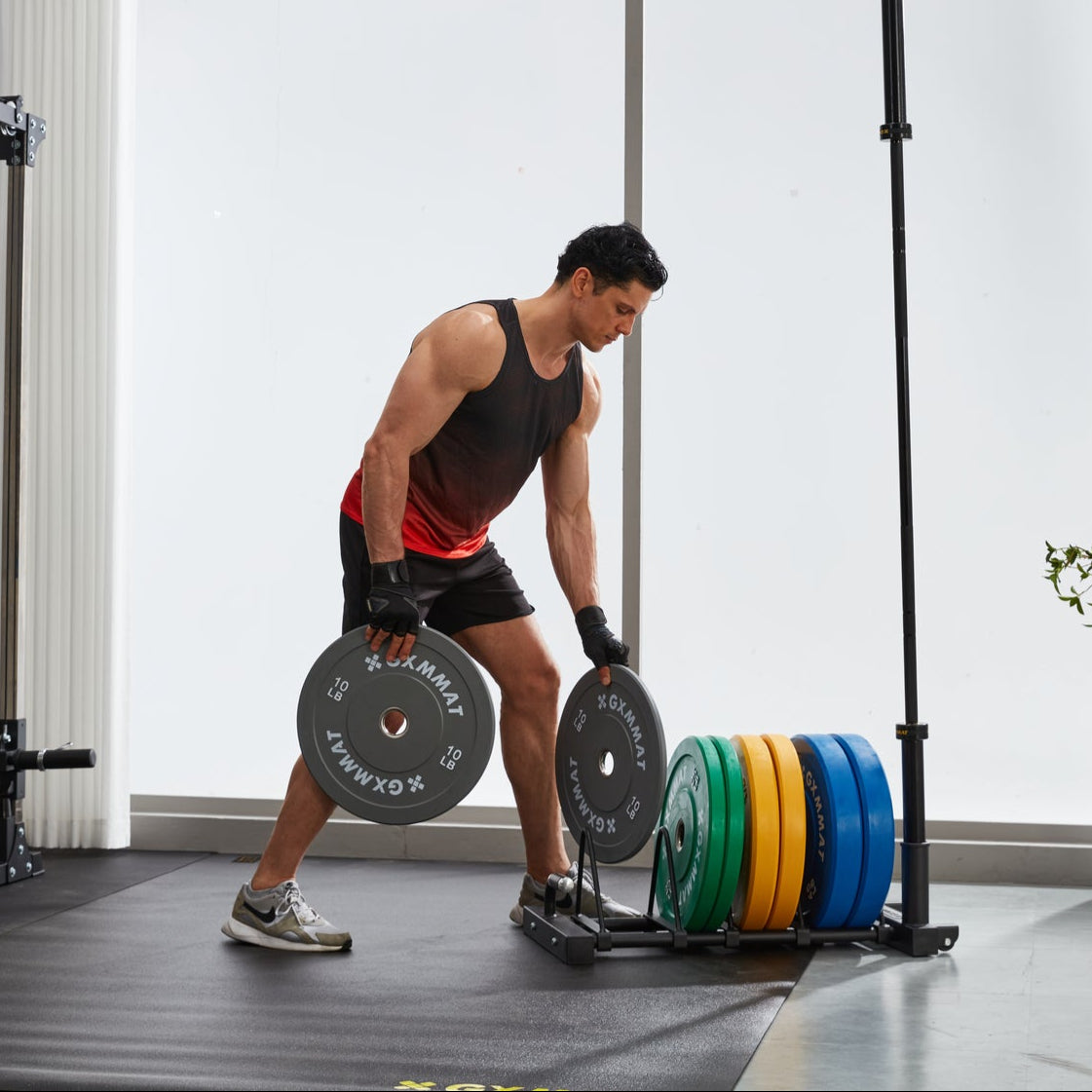 Man loading color-coded GXMMAT rubber bumper plates on a barbell