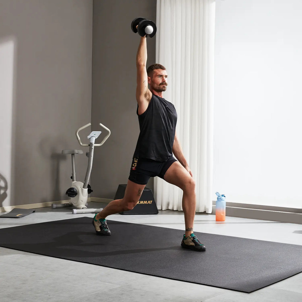 Man doing a single-arm dumbbell overhead lunge on a GXMMAT large exercise mat